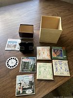 Full lot content showing vintage black Sawyer's View-Master viewer, 7 reel slide sets with various themes, and original storage boxes on wood floor.