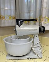 Vintage Sunbeam Mixmaster mixer mounted on base with two white mixing bowls, black and white body with chrome accents.