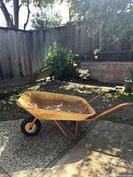 Side angle photo of the vintage wheelbarrow showing rusty metal tub and handles with black grips.