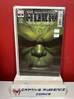 Image of 'The Immortal Hulk #18' comic book in plastic sleeve displayed against red background on a stand labeled 'CAPTIVE AUDIENCE COMICS'. Shows front cover artwork of Hulk's face.