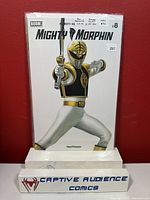 Photo of the Mighty Morphin Power Rangers #8 comic book with Bernardo White variant cover sealed in plastic against a red background with Captive Audience Comics display stand.