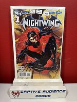 Photo of Nightwing #1 comic book showing front cover with Nightwing in black and red costume, DC Comics and New 52 logos visible. Comic is in protective sleeve with backing board.