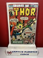 Photo of Thor #240 comic book in a protective plastic sleeve on a stand labeled 'Captive Audience Comics'. The cover shows vibrant art of Thor battling Loki.