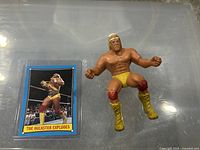 Photo of the 1985 Hulk Hogan Thumb Wrestler figure next to the 1987 Hulk Hogan trading card showing the wrestling action pose and the card's front.