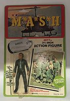 Front view of original card packaging showing the MASH logo, helicopter image, Hawkeye dog tag graphic, and sealed Hawkeye action figure in plastic bubble.