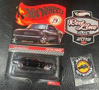 Photo showing one Hot Wheels 2018 Red Line Club Custom Camaro car in blister packaging, Red Line Club 2019 patch, and Mattel Hot Wheels button on a black surface.