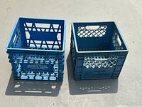 Photo shows two blue plastic milk crates side by side under sunlight, highlighting their lattice sides and handles.