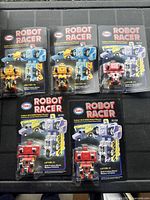 Five vintage Esso Robot Racer toys on original blister cards including red, yellow, blue, and purple robot variants, photographed from above showing full packaging and robot details.
