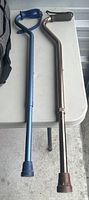 Two adjustable forearm canes on a white table, one blue and one bronze, showing general appearance