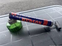 Full view of the vintage Hudson pest sprayer showing the green glass bottle attached to blue metal pump with red HUDSON lettering.