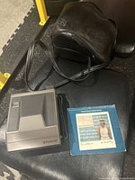 Photo showing the vintage Polaroid Spectra System camera, original black leather carrying case, and the camera manual laid out together.