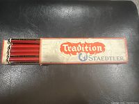 Original cardboard box with 11 red and black striped Staedtler Tradition pencils visible inside, showing vintage graphics and logo.
