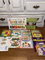 Photo showing an assortment of 13 workbooks, flashcards, and activity books focused on phonics, math, writing skills for Pre-K to Grade 1 children.