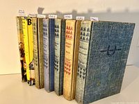 Seven hardcover books from the Famous Horse Stories series arranged in order of publication years from 1940 to 1952. Shows cloth bindings in blue and beige tones, some labeled with years on small paper tabs on top, some books have dust jackets.