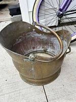 Front angled view of brass coal scuttle showing interior details and hinged handle resting down.