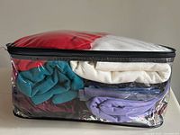 Clear plastic zippered bag filled with folded assorted fabric remnants in red, white, teal, purple, and multicolor, packed tightly together.