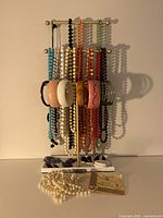 Photo showing assorted colorful beaded necklaces and bracelets Hanging on a jewelry stand. A pearl chain and Star Wars collectible pin in package are placed at the base.