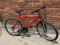 Full side view of the red CCM X Volt mountain bike leaning against a brick wall, showing frame, tires, seat, and handlebars.