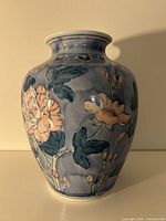 Front side of the hand-painted ceramic vase showing floral design and blue background under light