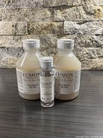 Three bottles displayed on a dark surface with a stone textured background: two larger 500 ml bottles labeled Pouring Resin, and one smaller 2 fl oz bottle labeled Cell Enhancer.