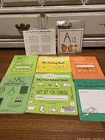 Layout of educational books from Handwriting Without Tears including My First School Book, My Printing Book, Preschool workbook, Power and Write notebook and gray block paper sheet on table.