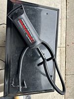 Black Intex manual air pump with flexible hose and multiple nozzle attachments placed on a black surface outdoors.