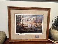 Framed print showing autumn forest pond scene with flying geese, hand signed, with commemorative stamp below print.