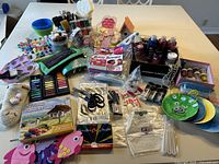 Overview of large mixed arts and crafts supplies on table including paints, brushes, craft foam shapes, glitter glue, bath bomb kit, and other miscellaneous items