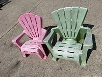 Two children's Adirondack chairs, one pink and one green, placed outside on concrete.