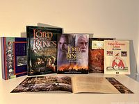 Five books displayed upright, showing cover art for The Lord of the Rings visual companion, making of movie trilogy book, The Hobbit, Father Christmas Letters, and a boxed or slipcase item.