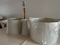 Lamp base with two lampshades side by side viewed from slightly above on table against neutral wall