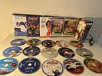 Photo of over 20 DVDs arranged on a surface showing front cover cases and multiple discs laid out