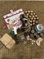 Top-down view of assorted Christmas and holiday craft items including ribbons, pinecones, gold bells, gift bags, and small decorations all laid out on a carpeted surface.