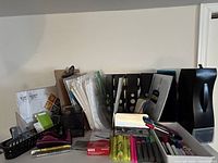 Overview of assorted office supplies including markers, pens, folders, binders, and paper on shelf