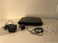 Black portable DVD player and two black power adapters with cords on white surface against wall