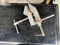 Front angle view of silver metal table bench vise showing screw mechanism and jaws with wooden inserts.