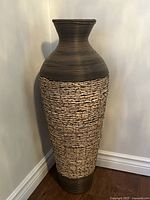 Large floor vase with brown resin top and base and natural wicker midsection, shown in corner of room.