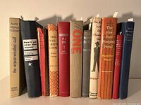 Front view of ten vintage hardcover books standing upright, showing spines with titles and authors.