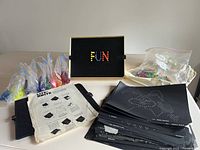 Full contents of the Lite-Brite set displayed on table: black peg board with peg holes, color-sorted pegs in plastic bags, multiple black design templates, instruction sheet. The peg board spells 'FUN' with multi-colored pegs.