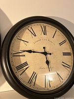 Front photo of the black framed wall clock showing Roman numerals and brand name Edinburgh Clockworks Co London England on cream antique white background