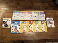 Photo showing the five sliding card volumes, Parents' Guide, stack of early reading books, and a set of teaching cards arranged side by side on wood floor.
