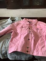 Two Azur brand jean jackets laid flat on a table, one pink and one light blue/grey, showing front button closures and chest pockets.