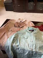 Five large size denim jackets from Azur displayed on table in different colors: peach, mint green, olive green, red, and light blue.