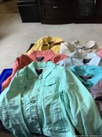 Seven small Azur jean jackets in various colors displayed on a carpeted floor showing front button details and collars