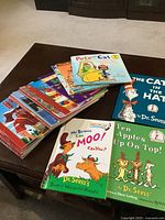 Photo showing a stack of approximately 10+ children’s books including Dr. Seuss’s 'Pete the Cat: Construction Cat', 'Mr. Brown Can Moo! Can You?', and 'Ten Apples Up On Top!'