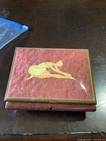 Top view of the rectangular ballerina music box with a pink velvet surface and a yellow ballerina figure stretching in the center.