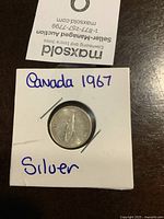 Top view of the 1967 silver Canadian dime in white coin holder with clear protective window and handwritten label 'Canada 1967 Silver'.