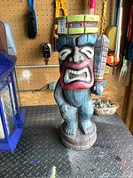Front view of the ceramic tiki statue showing detailed colorful facial features, headdress, and standing posture on circular base.