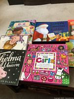 Books laid out on a carpeted floor, including Shelma the Unicorn, Treasure Hunt for Girls, Santa's Special Letter, Doc McStuffins, and several other children's books.