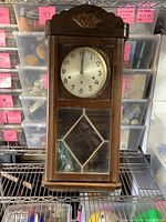 Front view of the vintage wooden wall clock showing the clock face and glass door with pendulum inside.